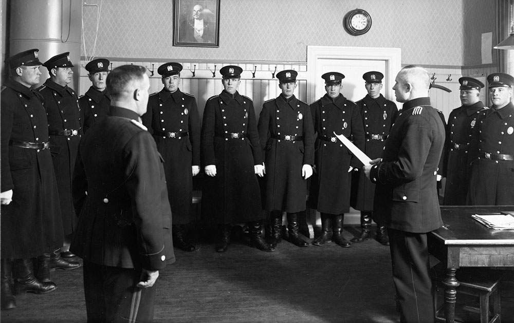 Throughout the 1930s, the overcoat for winter use remained a greatcoat with buttons in two rows. In winter, officers wore a uniform cap if the weather was warm and a fur cap on cold days. In 1935, a navy-style cap was substituted for the fur cap. The silver or light blue seam cords forming a cross on the dark blue cap cover revealed the rank of the bearer. Constables of the Turku Police Department at a briefing in the mid-1930s.