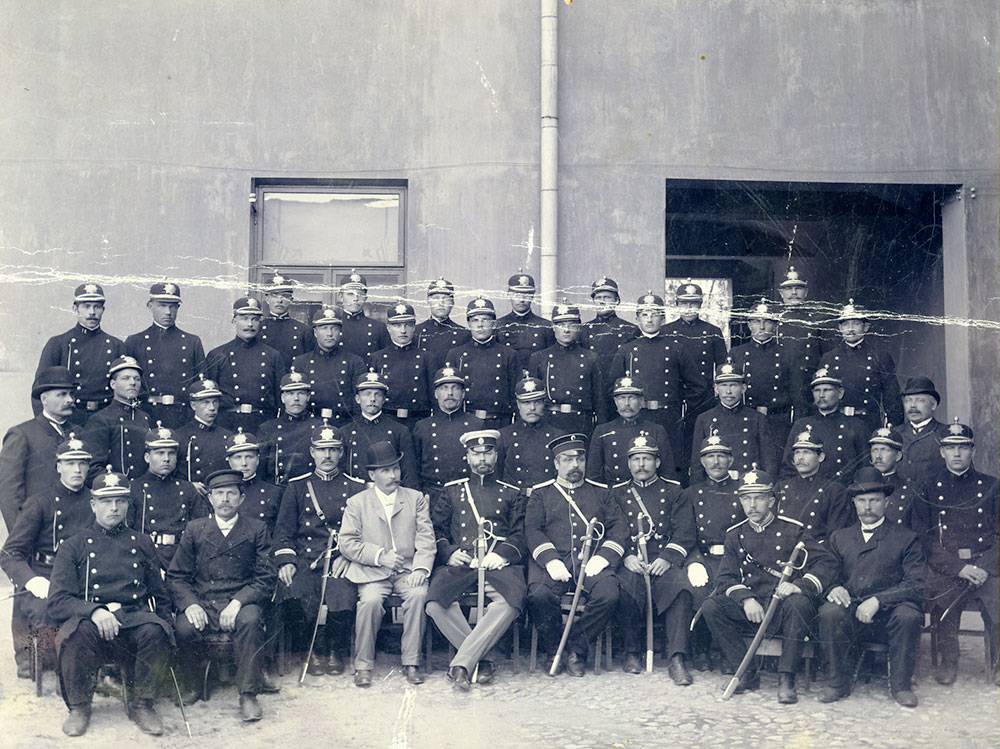 Poliisin 1900-luvun alussa käyttämien housujen leikkausta ei asetuksissa tarkasti määritelty. Säädetty väri sen sijaan vaihteli voimassa olevasta asetuksesta ja virka-asemasta riippuen eikä vastannut aina virkatakin väriä. Vyö saattoi olla virkapuvun väristä kangasta tai nahkaa. Miekkaa varten oli yleensä erillinen nahkainen olkakannatin. Oulun poliiseja vuonna 1908, yllään virkapuku m1906. Kuvaaja: F. Suomela.